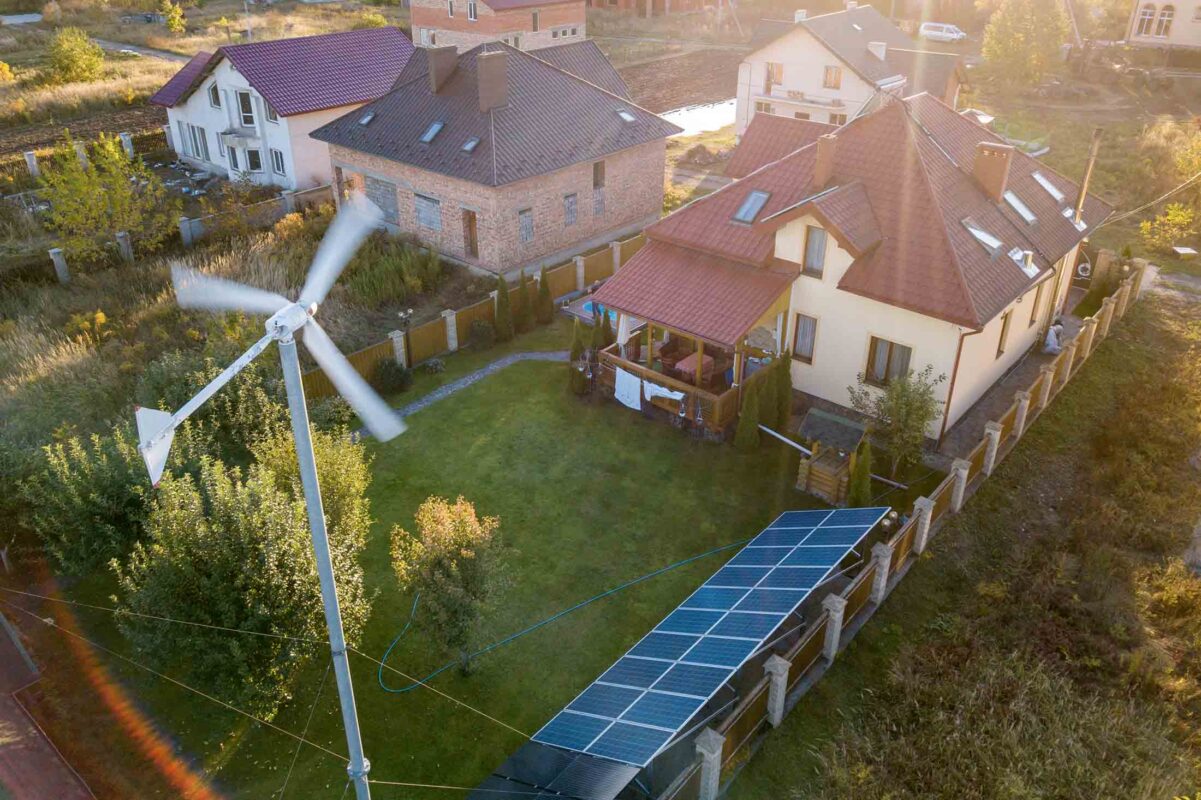 Aerial view of a residential private house with solar panels on roof and wind generator turbine.