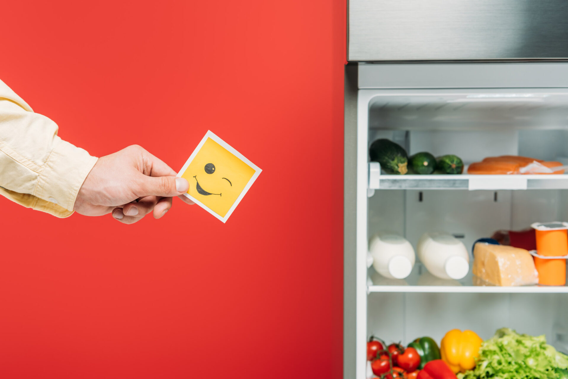 cropped view of man holding smiley face near open fridge with fr