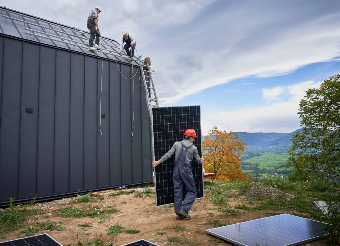 Technicians carrying photovoltaic solar module while installing solar panel system on roof of house