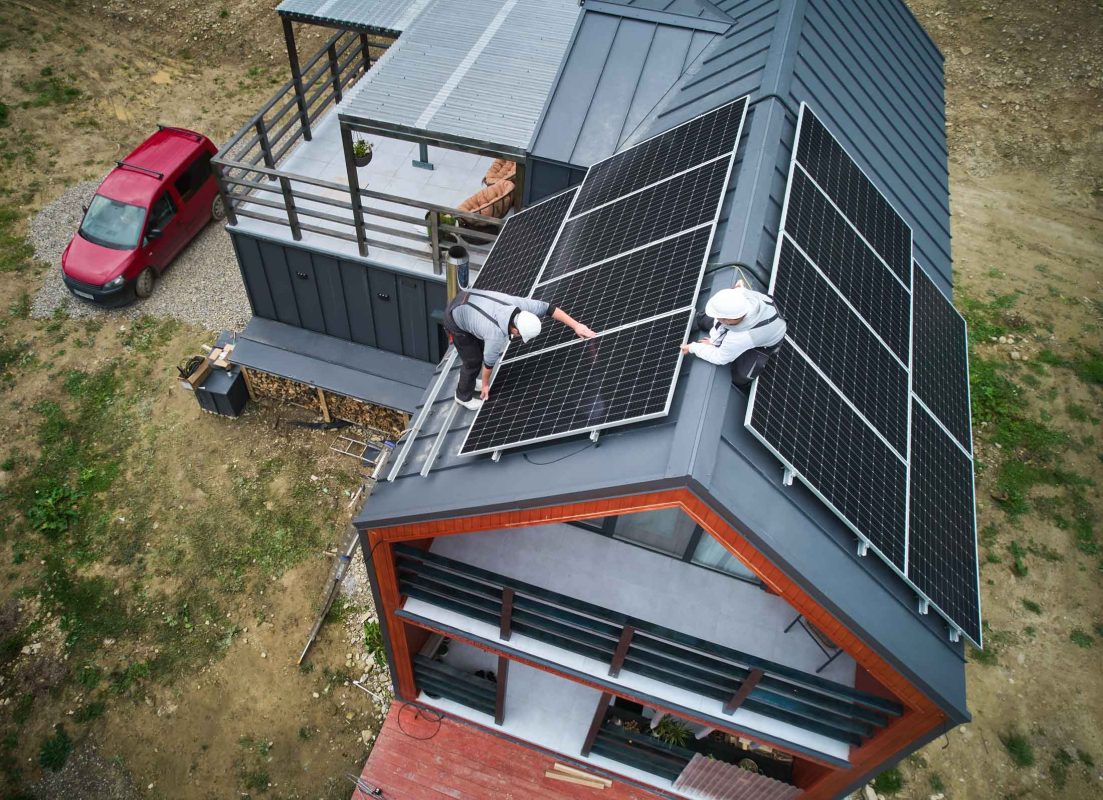 Men workers installing solar panels on roof of house.